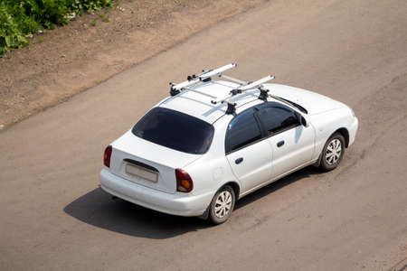 View from above of new shiny white expensive car with dark windows and luggage on roof moving along...