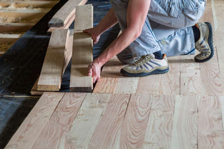 Close up of professional carpenter installing natural wooden new planks on cement floor in empty unfinished room under reconstruction. Improvement, renovation and carpentry concept.の写真素材