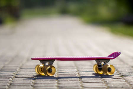 Close-up of child plastic pink skateboard isolated on pavement against bright white and green blurred bokeh background. Sport, recreation, fun and plays concept.の写真素材