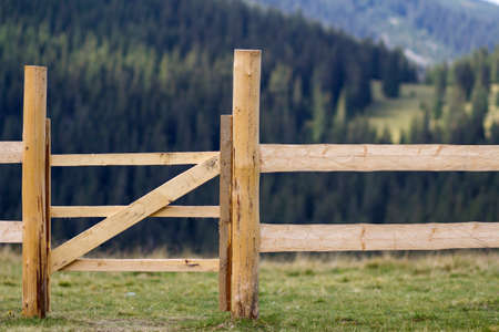 Close-up of low rough wooden fence on lit by bright summer sun grassy valley on Carpathian mountains...