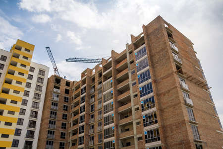 High rising multistory residential apartment brick building and working crane on block under...