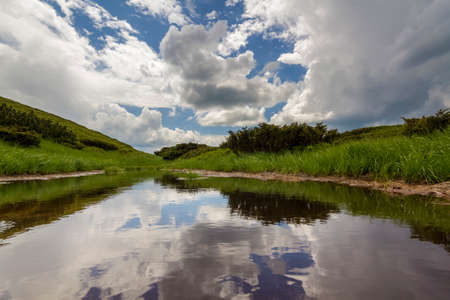 Beautiful peaceful summer view of bright blue sky with lit by sun white puffy clouds reflected in...