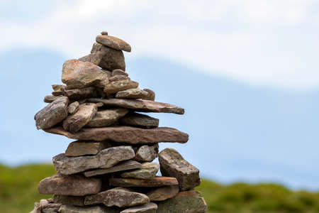 Lit by bright summer sun uneven mountain stones stacked and balanced like pyramid pile on green grassy valley on light white blue copy space sky background. Tourism. Traveling and landmark concept.の写真素材