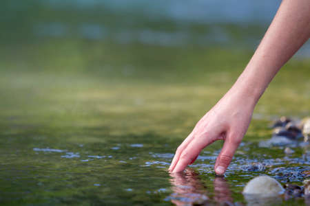Close-up of beautiful white woman hand tenderly touching, scooping clean fresh sweet water on blurred green copy-space background. Tourism, active lifestyle, nature and pollution problems concept.の写真素材
