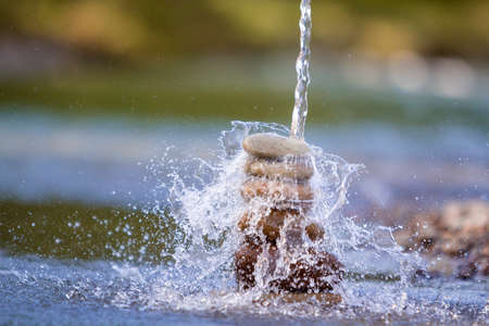 Close-up abstract image of water pouring down on rough natural brown uneven different sizes and forms stones balanced like pyramid pile landmark on blurred blue-green misty copy space background.の写真素材