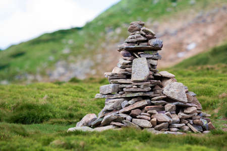 Lit by bright summer sun uneven mountain stones stacked and balanced like pyramid pile on green grassy valley on light white blue copy space sky background. Tourism. Traveling and landmark concept.の写真素材