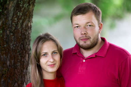 Close-up portrait of young attractive happy romantic smiling couple in love, pretty blond long-haired girl and handsome unshaven man hugging together outdoors on bright blurred sunny background.の写真素材