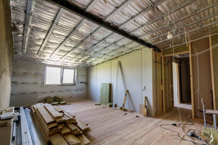 Big empty room under construction and renovation with silver aluminum foil on walls and ceiling, electrical wires output, oak floor and drywall. Professional reconstruction and insulation concept.の写真素材