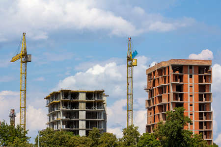 New modern high apartment buildings under construction among green tree tops. Tower crane silhouette...