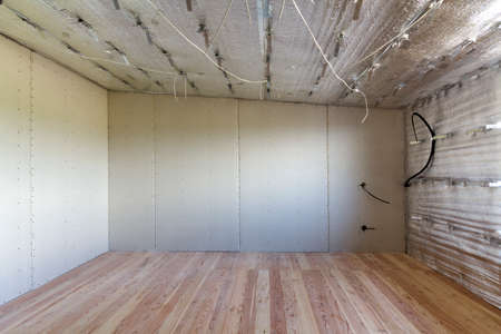 Big empty room under construction and renovation with silver aluminum foil on walls and ceiling, electrical wires output, oak floor and drywall. Professional reconstruction and insulation concept.の写真素材