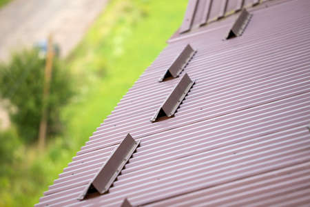 Close-up detail of metal brown shingle tiling house roof surface with rain gutter pipe and snow guards protective fence. Professional work, safety, construction, renovation and durability concept.の写真素材