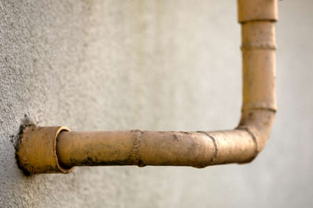Close-up detail of old dirty painted yellow natural gas pipes with welding seams on white gray residential house wall. Safety, danger, old and modern technology concept. Copy space background.の写真素材