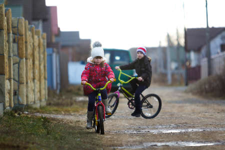 Two happy children boy and girl riding bicycles outdoors in cold weatherの写真素材