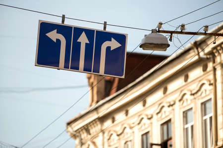 Close-up of road sign attached to trolley line near the lamp high over street with three white arrows on blue background showing direction of transportation moving. Order, choice and rules concept.のeditorial素材