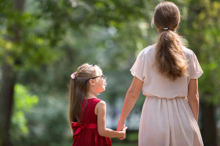Back view of small blond long-haired child girl with slender slim mother in fashionable dresses...