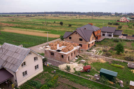 Aerial view of rural land for development in green field. New not finished brick houses and building sites on background of distant city and trees on horizon. Construction and real property concept.のeditorial素材