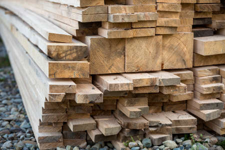 Close-up of piled stack of natural brown uneven rough wooden boards lit by bright sun. Industrial...