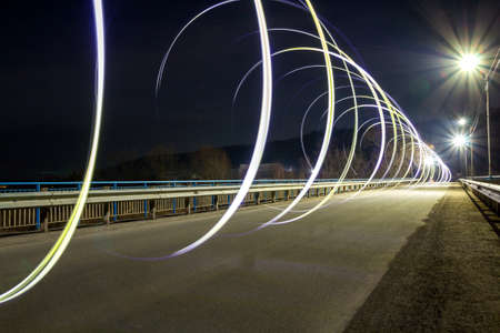 Brightly illuminated straight asphalt empty road stretching to distant woody hills on horizon on bright blue summer night sky copy space background. Speed and traveling concept.のeditorial素材