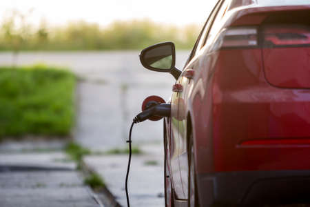 KYIV, UKRAINE - April 9, 2018: Close-up detail of shiny electric car being recharged on bright sunny suburb street background. Charger cable plugged to socket. Modern ecofriendly technology concept.のeditorial素材