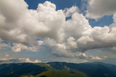 Fantastic panorama view of bright white puffy clouds lit by sun spreading against deep blue summer sky over green mountain ridge. Beauty and power of nature, meteorology and climate changing concept.の写真素材