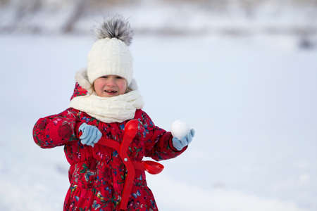 Cute little young funny toothless child girl in warm clothing playing having fun making snowballs on...