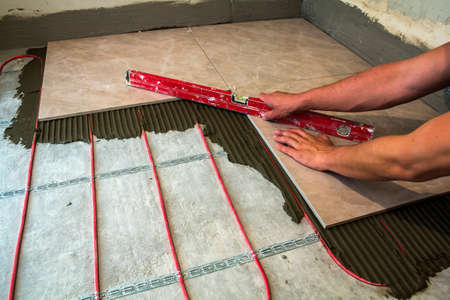 Ceramic tiles and tools for tiler. Worker hand installing floor tiles. Home improvement, renovation - ceramic tile floor adhesive, mortar, level.の写真素材