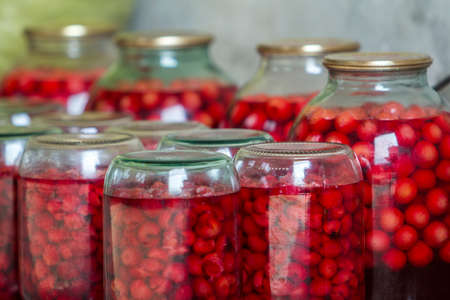 Close-up of glass jars with ripe red juicy sweet cherries covered with metal lids upside down on...