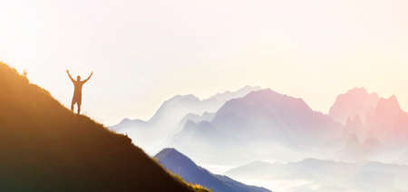 Man on peak of mountain. Emotional scene. Young man with backpack standing with raised hands on top...