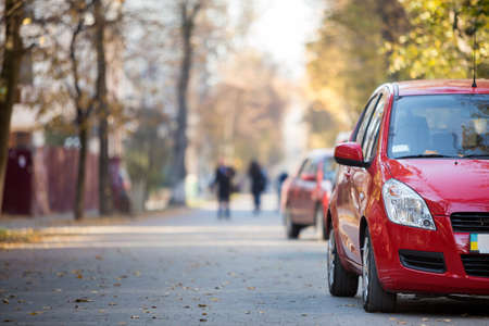 Close-up front view detail of bright red shiny car parked on pavement on background of blurred...