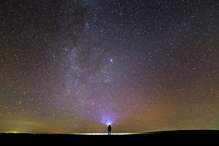 Back view of man with head flashlight standing on green grassy field under beautiful dark blue...
