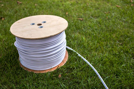 Top view of roll of white industrial electrical cable on large wooden reel isolated outdoors on green grass. Professional construction site cable, reliable wiring and durability.の写真素材