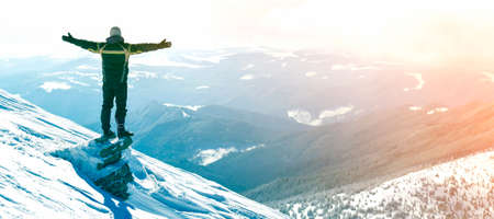 Silhouette of alone tourist standing on snowy mountain top in winner pose with raised hands enjoying...