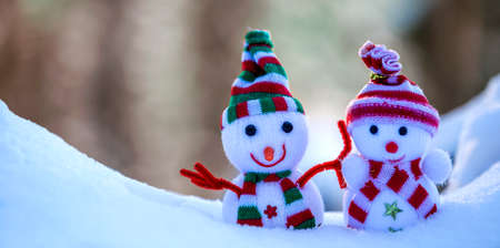 Two small funny toys baby snowman in knitted hats and scarves in deep snow outdoors on bright blue and white copy space background. Happy New Year and Merry Christmas greeting card.の写真素材