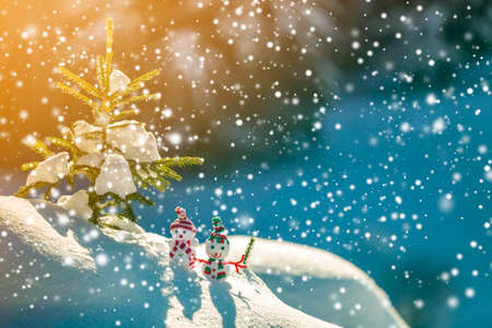 Two small funny toys baby snowman in knitted hats and scarves in deep snow outdoors near pine tree...