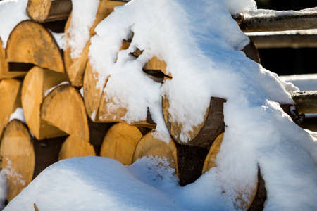 Neatly piled stack of chopped dry trunks wood covered with snow outdoors on bright cold winter sunny...