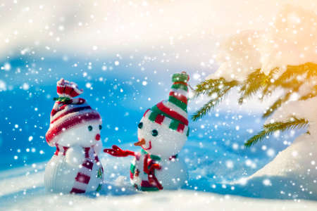 Two small funny toys baby snowman in knitted hats and scarves in deep snow outdoors on bright blue and white copy space background. Happy New Year and Merry Christmas greeting card.の写真素材