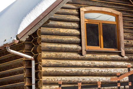 Close-up of corner of new wooden warm ecological cottage house roof covered with snow with steel gutter rain system. Professional construction and drainage pipes installation and connection concept.の写真素材