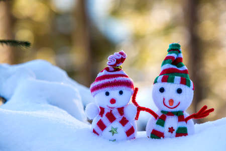 Two small funny toys baby snowman in knitted hats and scarves in deep snow outdoors on bright blue and white copy space background. Happy New Year and Merry Christmas greeting card.の写真素材