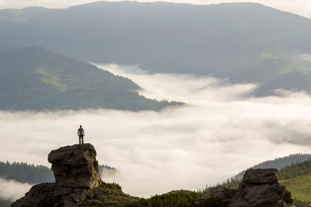 Silhouette of athletic climber tourist on high rocky formation on mountain valley filled with white...