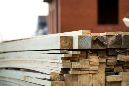 Stack of natural brown uneven rough wooden boards on building site. Industrial timber for carpentry, building, repairing and furniture, lumber material for roofing construction.の写真素材