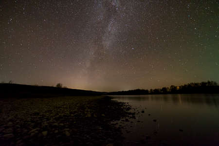 Peaceful landscape panorama at night. Long exposure shot of pebbles river bank, trees on horizon,...