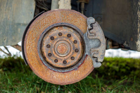 Close-up of old forsaken abandoned rusty broken trash car brake disc detail without rubber tire outdoors in field.の写真素材