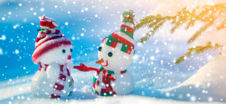 Two small funny toys baby snowman in knitted hats and scarves in deep snow outdoors on bright blue and white copy space background. Happy New Year and Merry Christmas greeting card.の写真素材