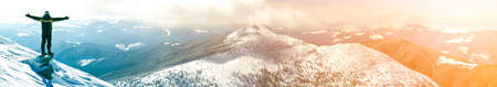 Silhouette of alone tourist standing on snowy mountain top in winner pose with raised hands enjoying view and achievement on bright sunny winter day. Adventure, outdoors activities, healthy lifestyle.の写真素材