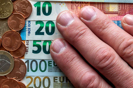 Hand fingers on background of neatly arranged stack of euro banknotes, currency bills worth ten,...