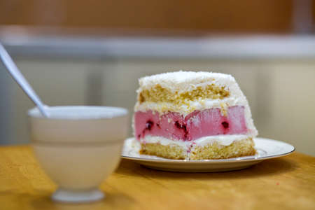 White plate with fresh delicious yummy homemade piece of fruit biscuit white and pink creamy cake on kitchen table at porcelain cup on light blurred copy space background.の写真素材