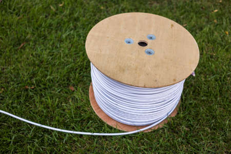 Top view of roll of white industrial electrical cable on large wooden reel isolated outdoors on green grass. Professional construction site cable, reliable wiring and durability.の写真素材