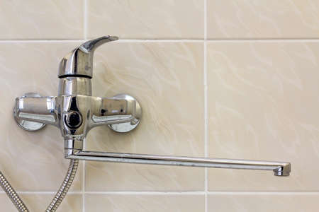 Water tap, chrome stainless metal faucet connected to shower stall tiled wall, mixer cold hot water on blurred bathroom copy space background. Modern home interior.の写真素材