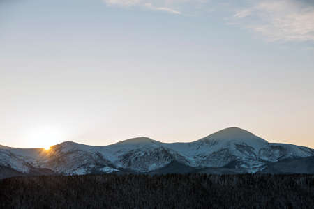 Winter mountains landscape panorama at sunrise. Clear blue sky over dark spruce pine trees forest, covered with snow mountain ridge peaks, bright rays of raising sun at dawn.の写真素材