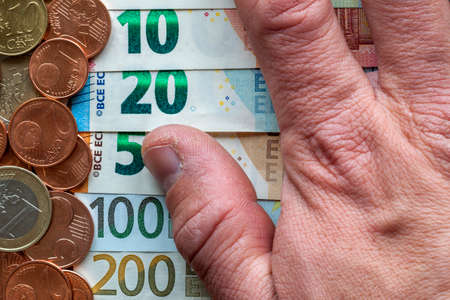 Hand fingers on background of neatly arranged stack of euro banknotes, currency bills worth ten,...